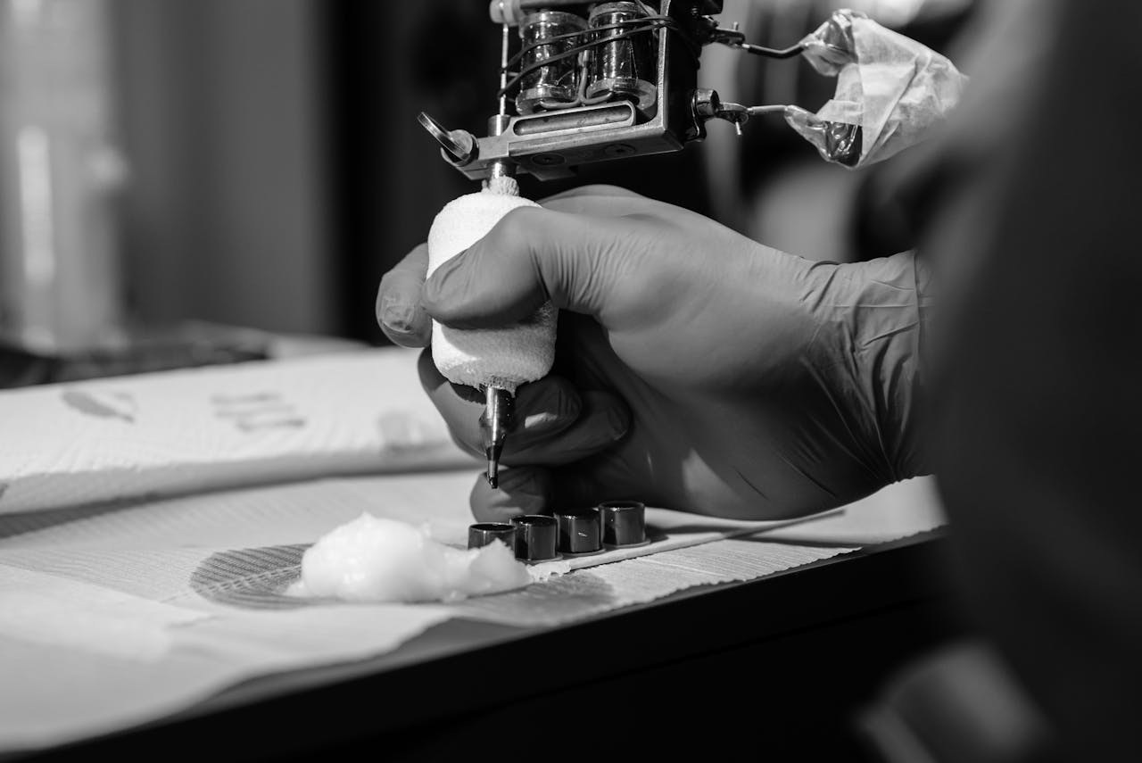 Detailed black and white close-up of a tattoo artist using a tattoo machine on a client's skin.
